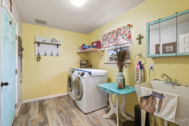 washroom featuring visible vents, light wood-style flooring, a sink, washer and dryer, and laundry area