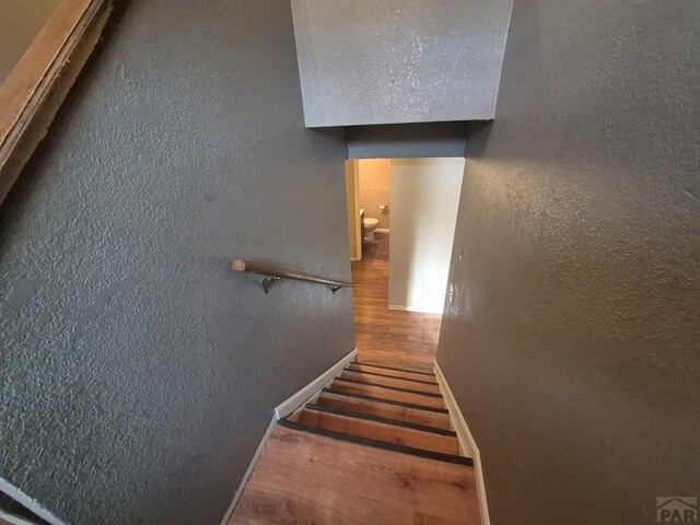 stairs with a textured wall, baseboards, and wood finished floors