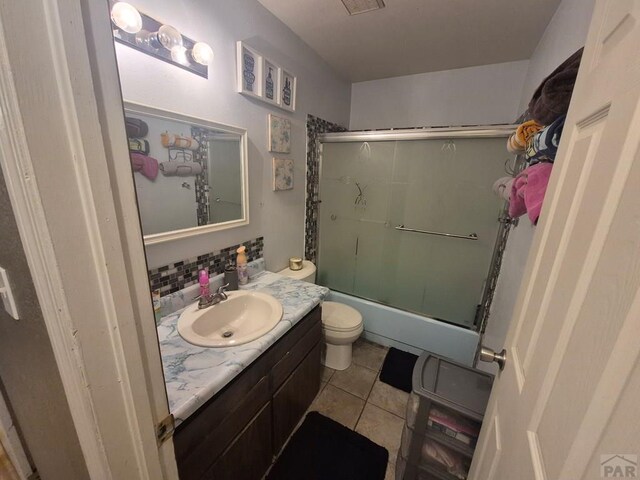 bathroom with toilet, shower / bath combination with glass door, tile patterned flooring, vanity, and backsplash