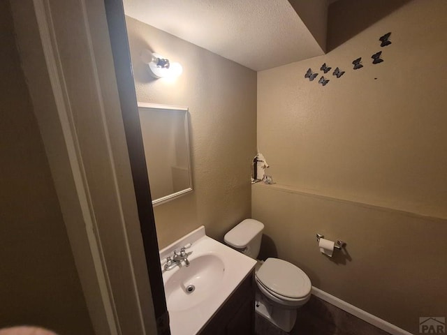 half bathroom featuring toilet, vanity, and baseboards