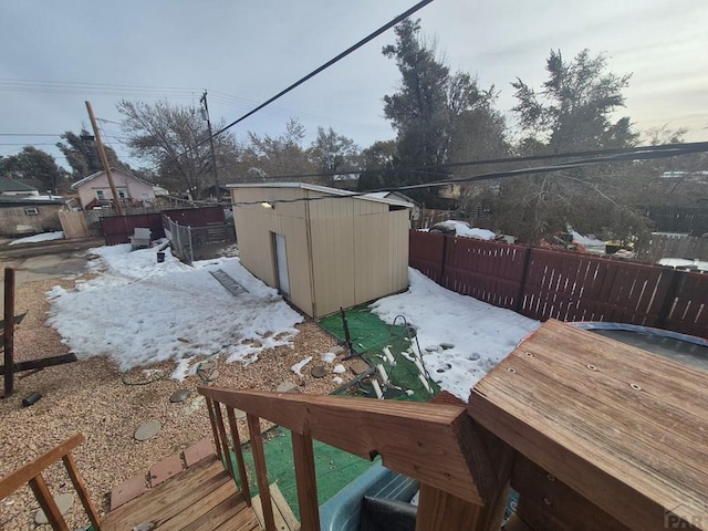 snow covered deck featuring a storage unit, an outdoor structure, and a fenced backyard