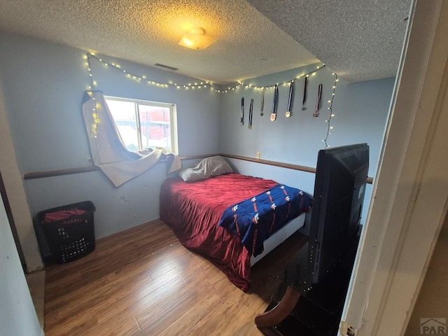 bedroom featuring visible vents, a textured ceiling, and wood finished floors