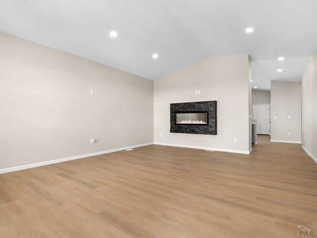 unfurnished living room with recessed lighting, vaulted ceiling, a stone fireplace, light wood-type flooring, and baseboards