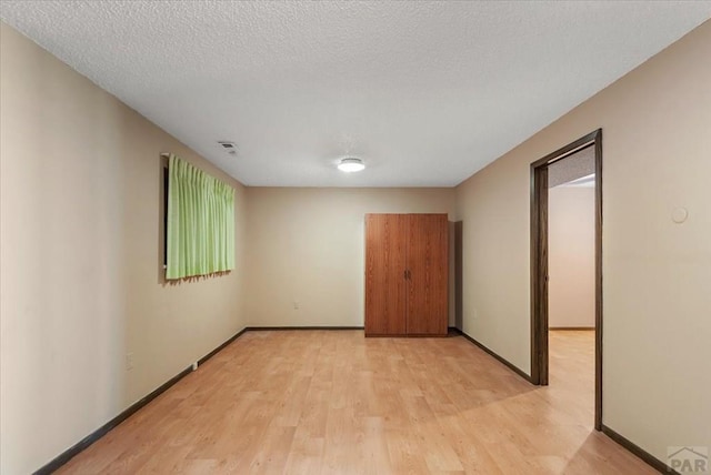 spare room with visible vents, light wood-style floors, baseboards, and a textured ceiling