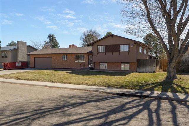 tri-level home featuring brick siding, a front lawn, fence, concrete driveway, and an attached garage