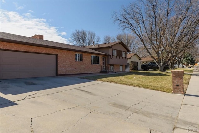 tri-level home with a front lawn, concrete driveway, an attached garage, brick siding, and a chimney