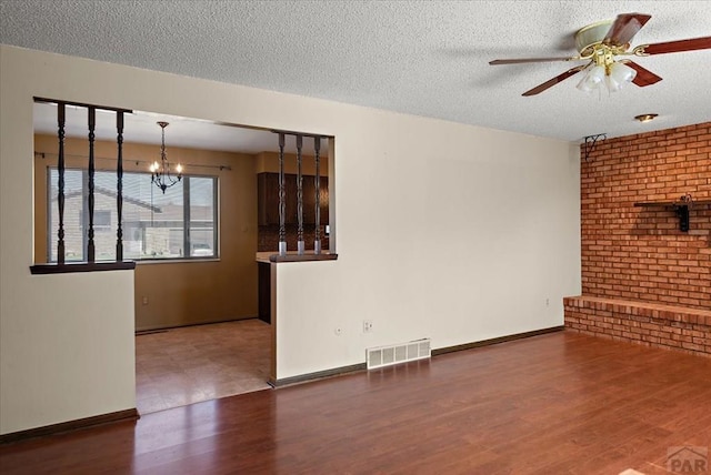 unfurnished living room with wood finished floors, baseboards, visible vents, a textured ceiling, and ceiling fan with notable chandelier