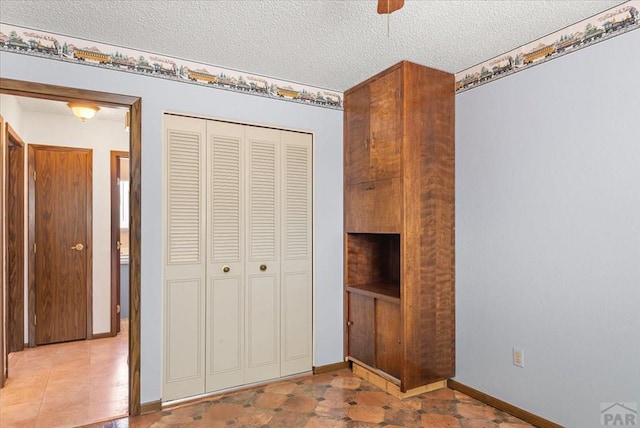 unfurnished bedroom with a ceiling fan, baseboards, a closet, and a textured ceiling