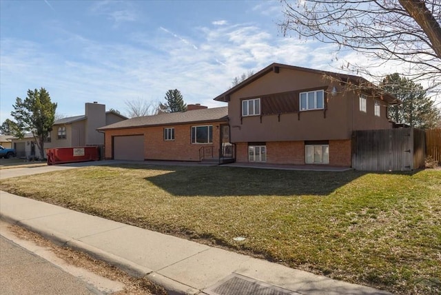 tri-level home with fence, concrete driveway, a front lawn, a garage, and brick siding