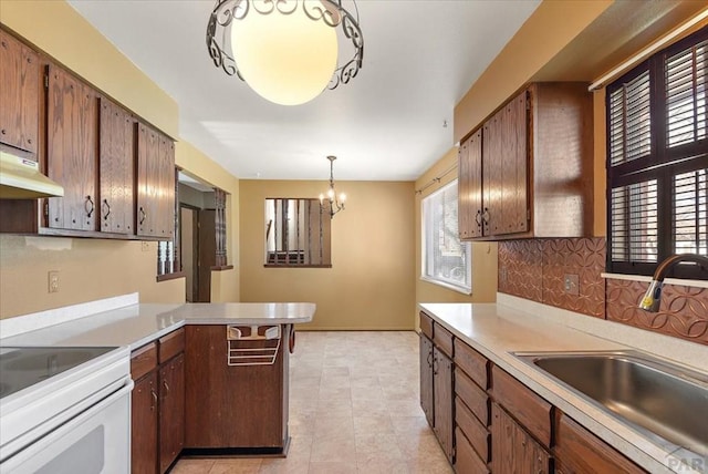 kitchen with a sink, decorative backsplash, light countertops, under cabinet range hood, and a chandelier