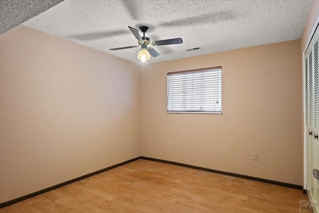 spare room featuring light wood-type flooring, baseboards, a textured ceiling, and ceiling fan