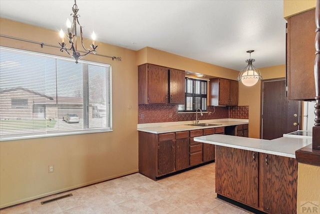 kitchen featuring tasteful backsplash, visible vents, light countertops, a peninsula, and a sink