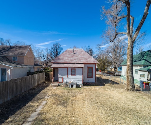 rear view of property with entry steps, fence, and a lawn