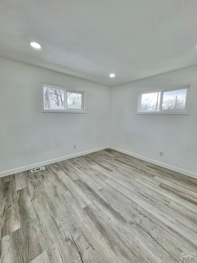 empty room with a wealth of natural light, wood finished floors, visible vents, and baseboards