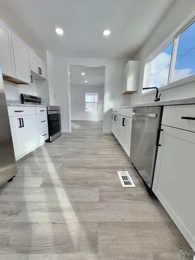 kitchen with light wood finished floors, light countertops, visible vents, appliances with stainless steel finishes, and white cabinetry