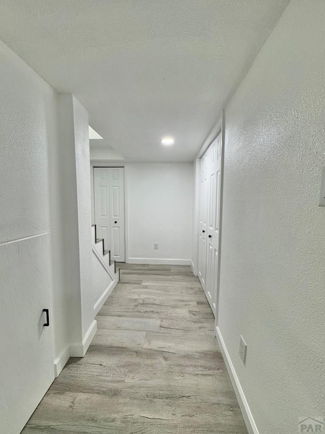 corridor with a textured wall, wood finished floors, and baseboards