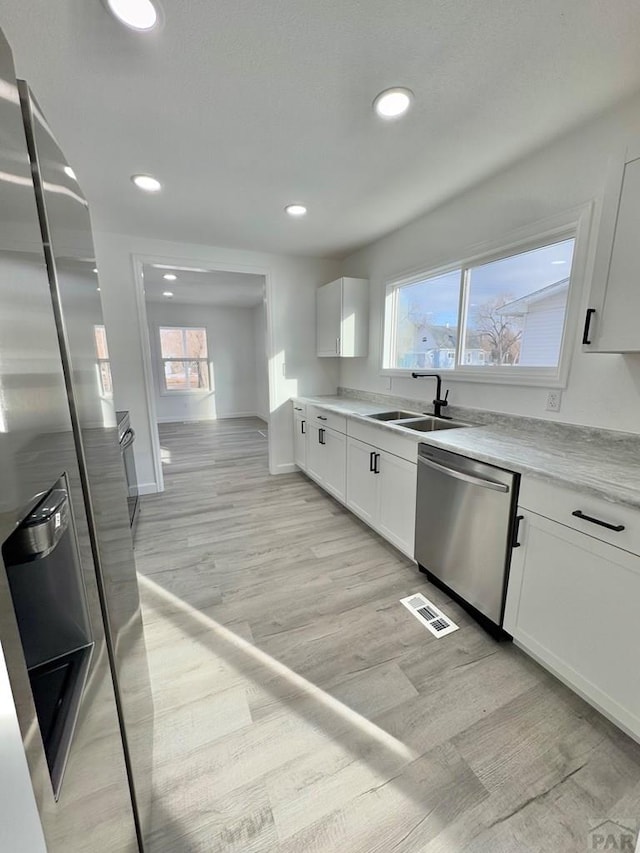 kitchen featuring light wood finished floors, visible vents, stainless steel dishwasher, white cabinets, and a sink