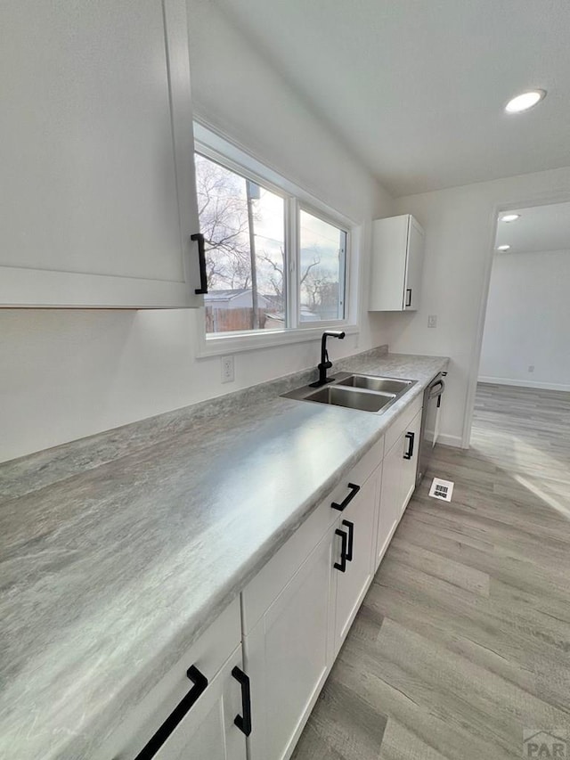 kitchen featuring white cabinets, dishwasher, light countertops, light wood-style floors, and a sink