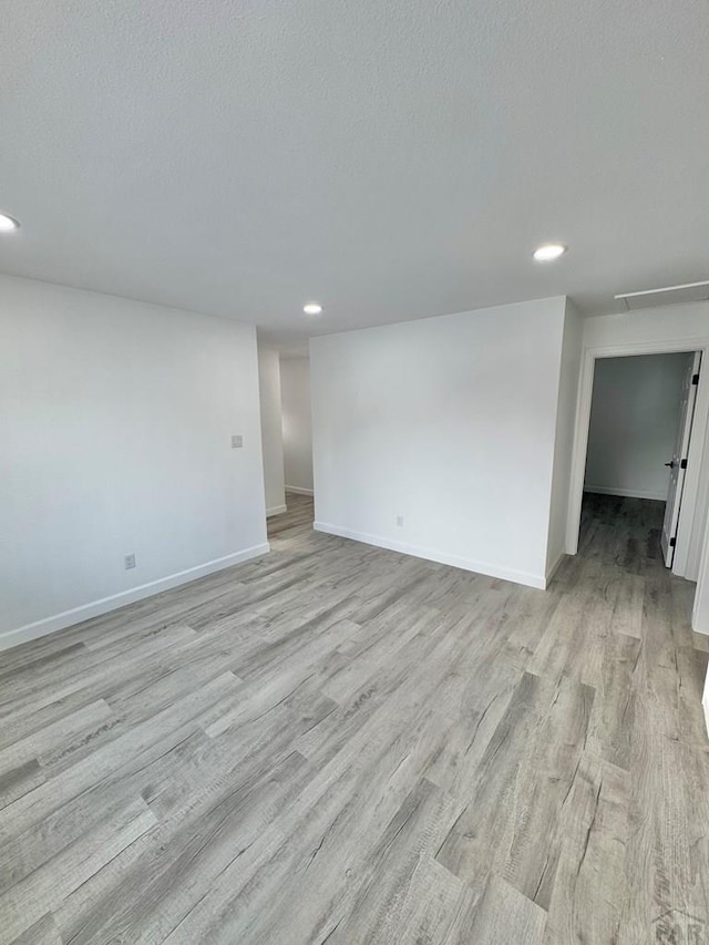 spare room with a textured ceiling, recessed lighting, light wood-style flooring, and baseboards