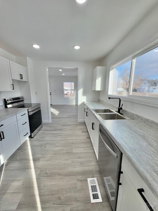 kitchen featuring visible vents, light wood-style flooring, stainless steel appliances, white cabinetry, and a sink