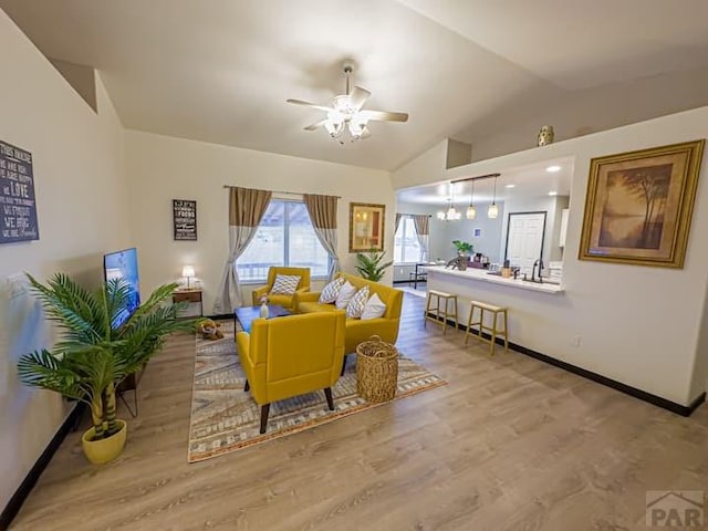 living area with a ceiling fan, vaulted ceiling, baseboards, and wood finished floors