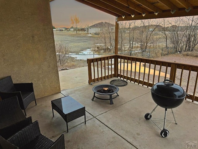 patio terrace at dusk with a fire pit, area for grilling, and fence