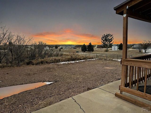 yard at dusk featuring fence, an outbuilding, and a patio