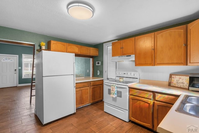 kitchen with tasteful backsplash, light countertops, white appliances, and under cabinet range hood