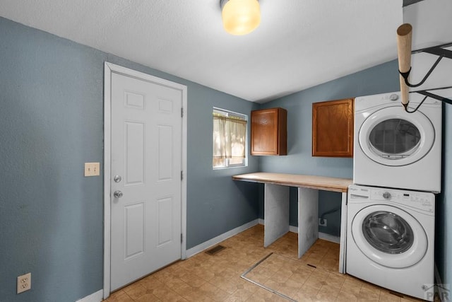 laundry area featuring visible vents, baseboards, cabinet space, and stacked washer / drying machine