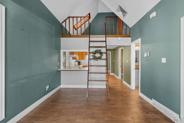 interior space with high vaulted ceiling, wood finished floors, visible vents, and baseboards