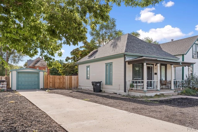 exterior space with a porch, a shingled roof, an outdoor structure, a detached garage, and driveway