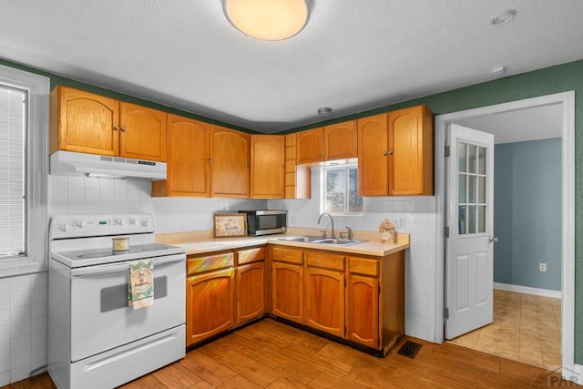 kitchen featuring electric range, stainless steel microwave, light countertops, under cabinet range hood, and a sink