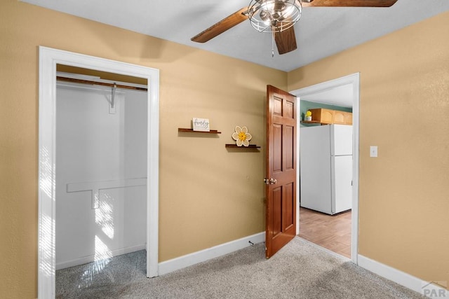 unfurnished bedroom with a closet, freestanding refrigerator, light carpet, ceiling fan, and baseboards