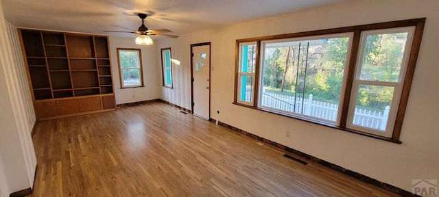 interior space featuring a ceiling fan, light wood-type flooring, visible vents, and baseboards