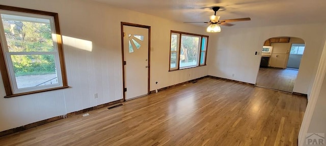 spare room with baseboards, visible vents, arched walkways, ceiling fan, and wood finished floors