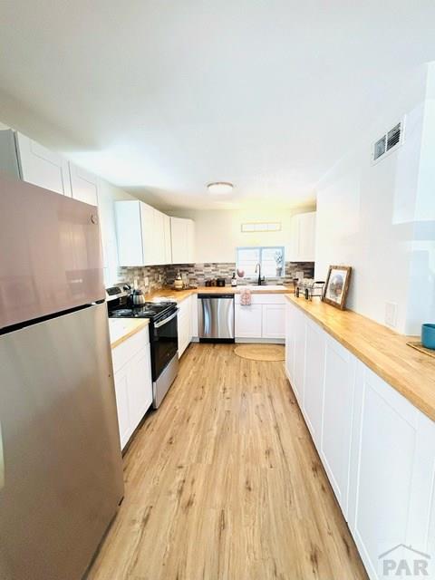 521 Tyler St, Pueblo, CO 81004 - kitchen with appliances with stainless steel finishes, white cabinets, light wood-style flooring, decorative backsplash, and butcher block countertops