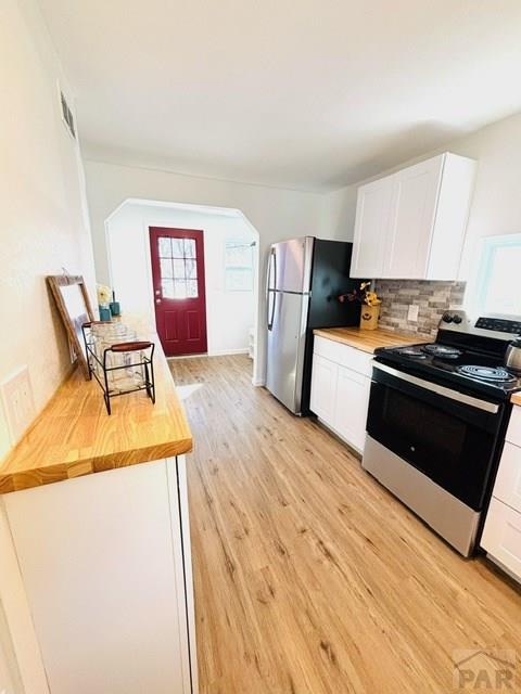 521 Tyler St, Pueblo, CO 81004 - kitchen with stainless steel appliances, wood counters, light wood-type flooring, white cabinetry, and arched walkways