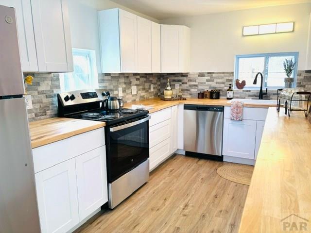 521 Tyler St, Pueblo, CO 81004 - kitchen with appliances with stainless steel finishes, butcher block counters, decorative backsplash, white cabinets, and light wood finished floors