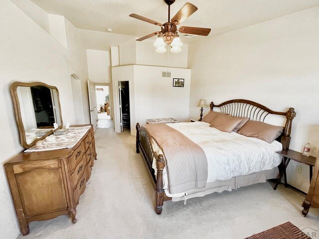 bedroom with light colored carpet, visible vents, a high ceiling, a ceiling fan, and a textured ceiling