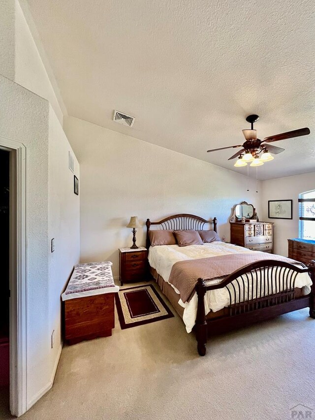 bedroom with a textured ceiling, light colored carpet, a ceiling fan, baseboards, and visible vents