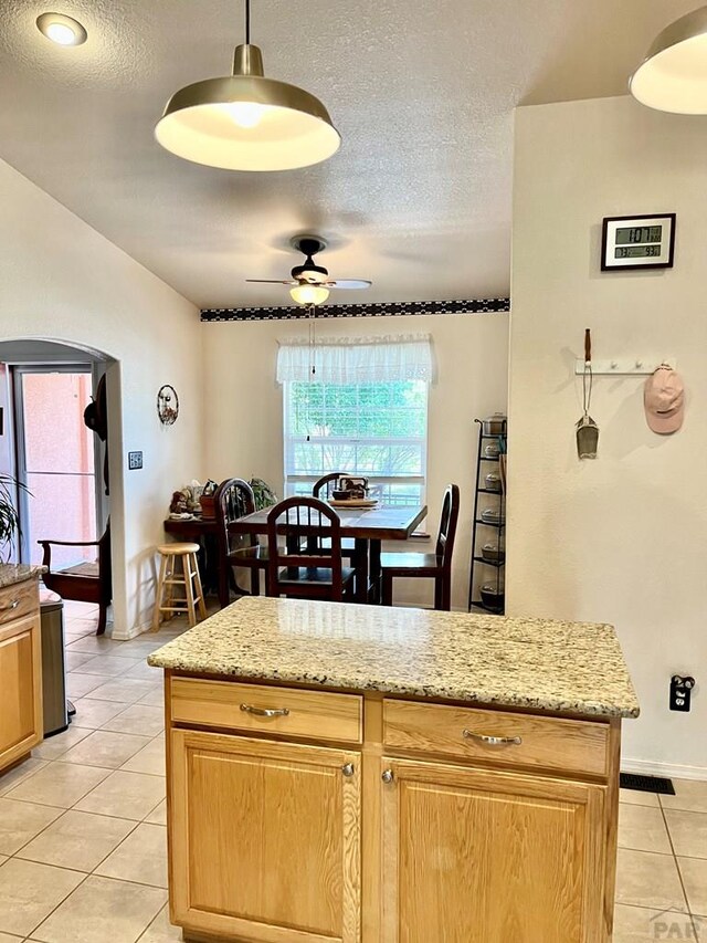 kitchen with light stone counters, light tile patterned floors, hanging light fixtures, ceiling fan, and a textured ceiling