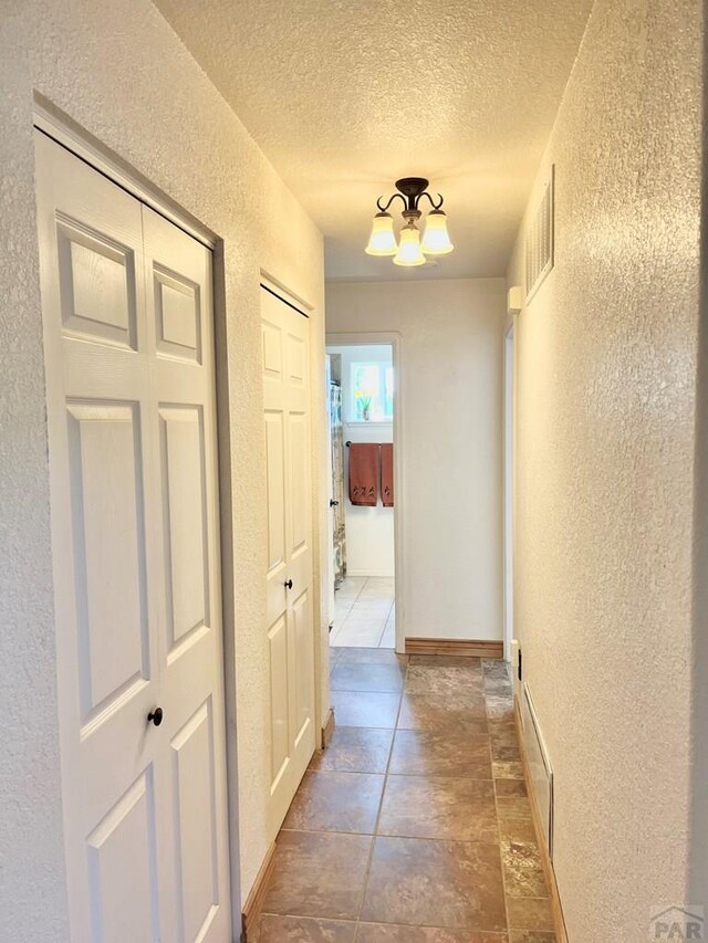 hallway featuring visible vents, a textured wall, a textured ceiling, and an inviting chandelier