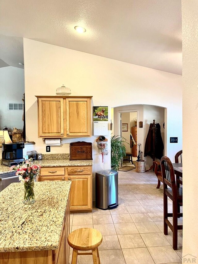 kitchen with light tile patterned floors, a textured ceiling, visible vents, and light stone countertops