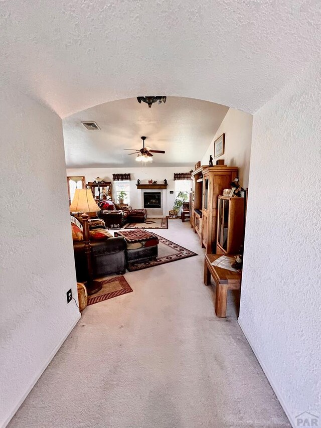 living room with carpet floors, visible vents, a textured wall, ceiling fan, and a textured ceiling