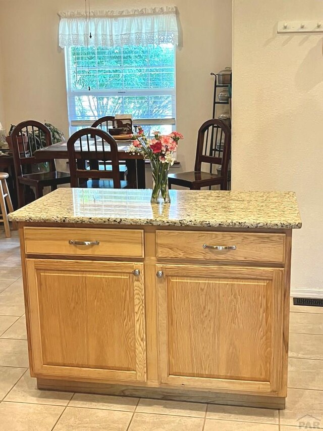 kitchen featuring a healthy amount of sunlight, light tile patterned floors, light stone counters, and brown cabinetry