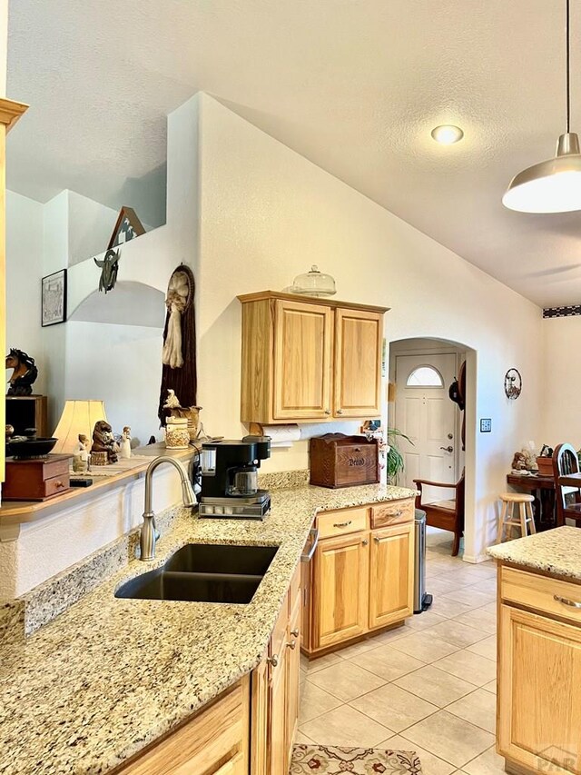 kitchen with lofted ceiling, light tile patterned floors, a sink, light stone countertops, and pendant lighting