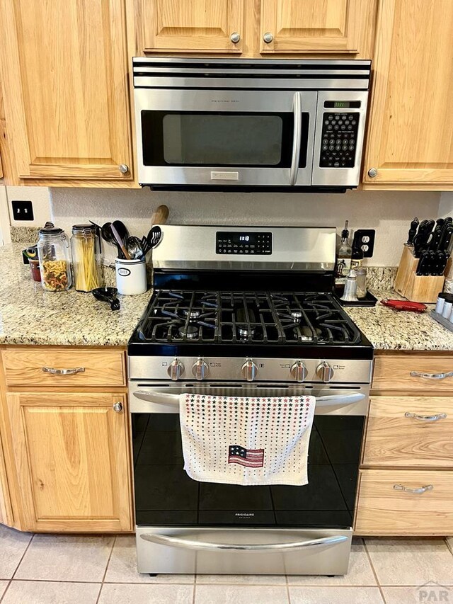 kitchen with light tile patterned floors, light stone counters, and stainless steel appliances