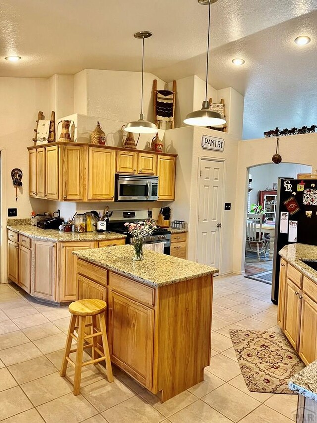 kitchen with light stone counters, pendant lighting, stainless steel appliances, light tile patterned flooring, and a kitchen island