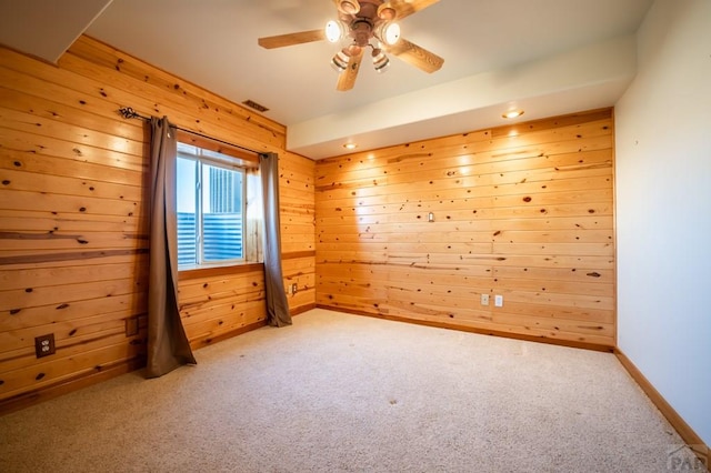 unfurnished room with wood walls, a ceiling fan, visible vents, baseboards, and carpet