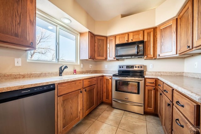 kitchen with stainless steel appliances, a sink, light countertops, and brown cabinets